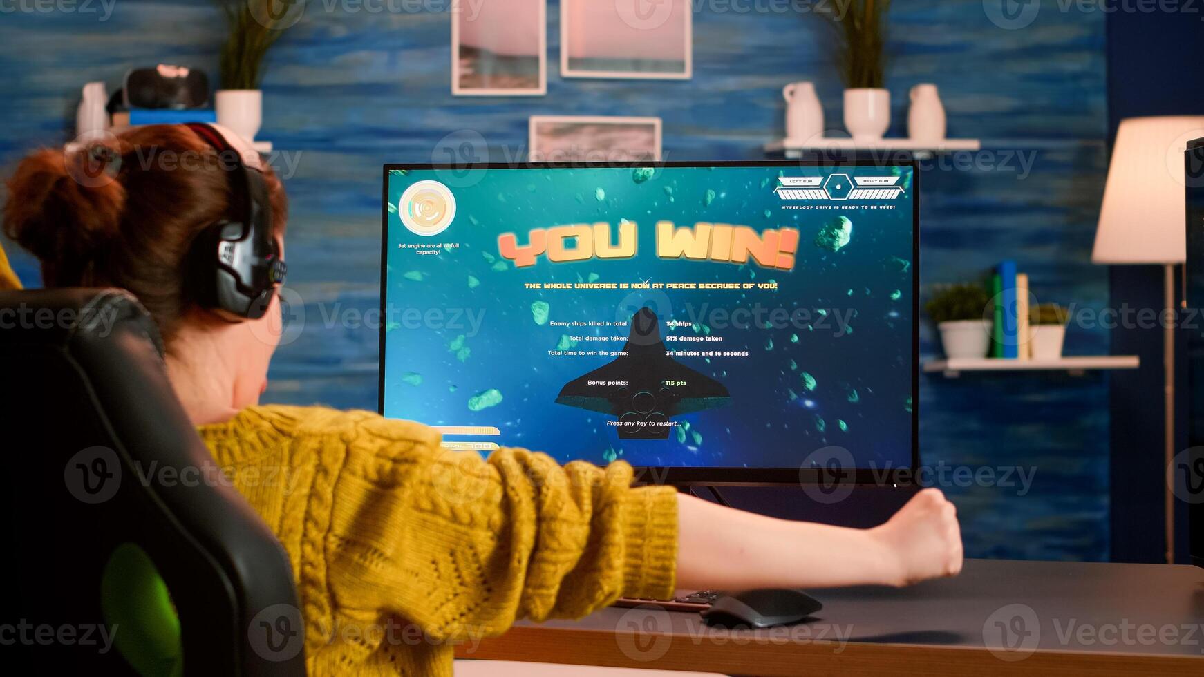 Back view of happy pro gamer winning space shooter game, raising hand celebrating, Virtual shooter game in cyberspace, esports player playing on computer game sitting at home, gaming tournament photo