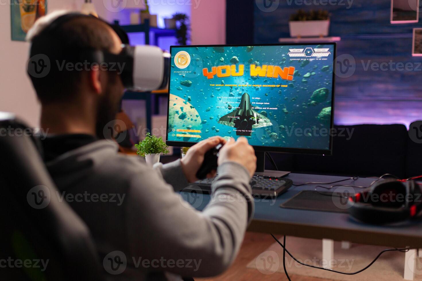 Gamer man winning space shooter game use virtual reality goggles. Competitive player using joystick for online championship sitting on gaming chair late at night playing on professional computer photo