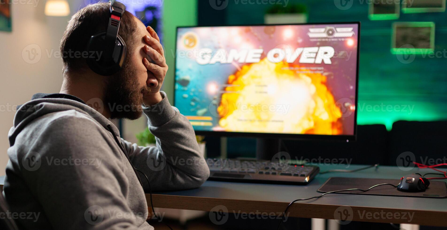 Gamer with headset and microphone losing games in gaming home studio and talking with friends on networks. Defeated man with headphones streaming online cyber performing during tournament photo