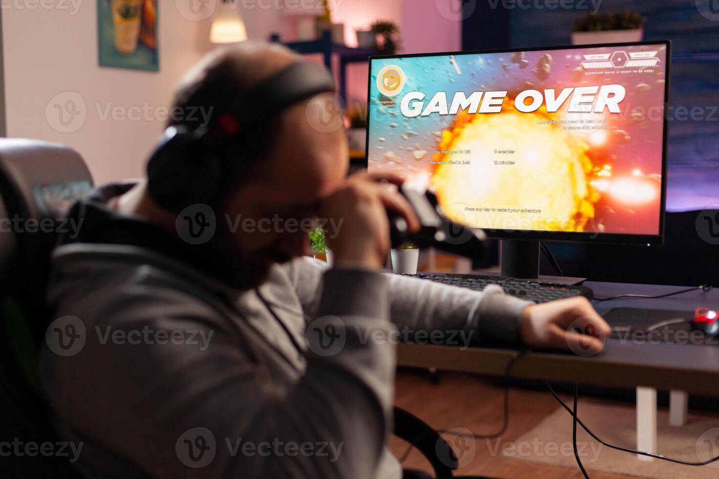 Addicted gamer losing space shooter videogame using headphones and wireless joystick. Upset player . Defeated gamer using professional equipment for online tournament late at night in gaming room photo