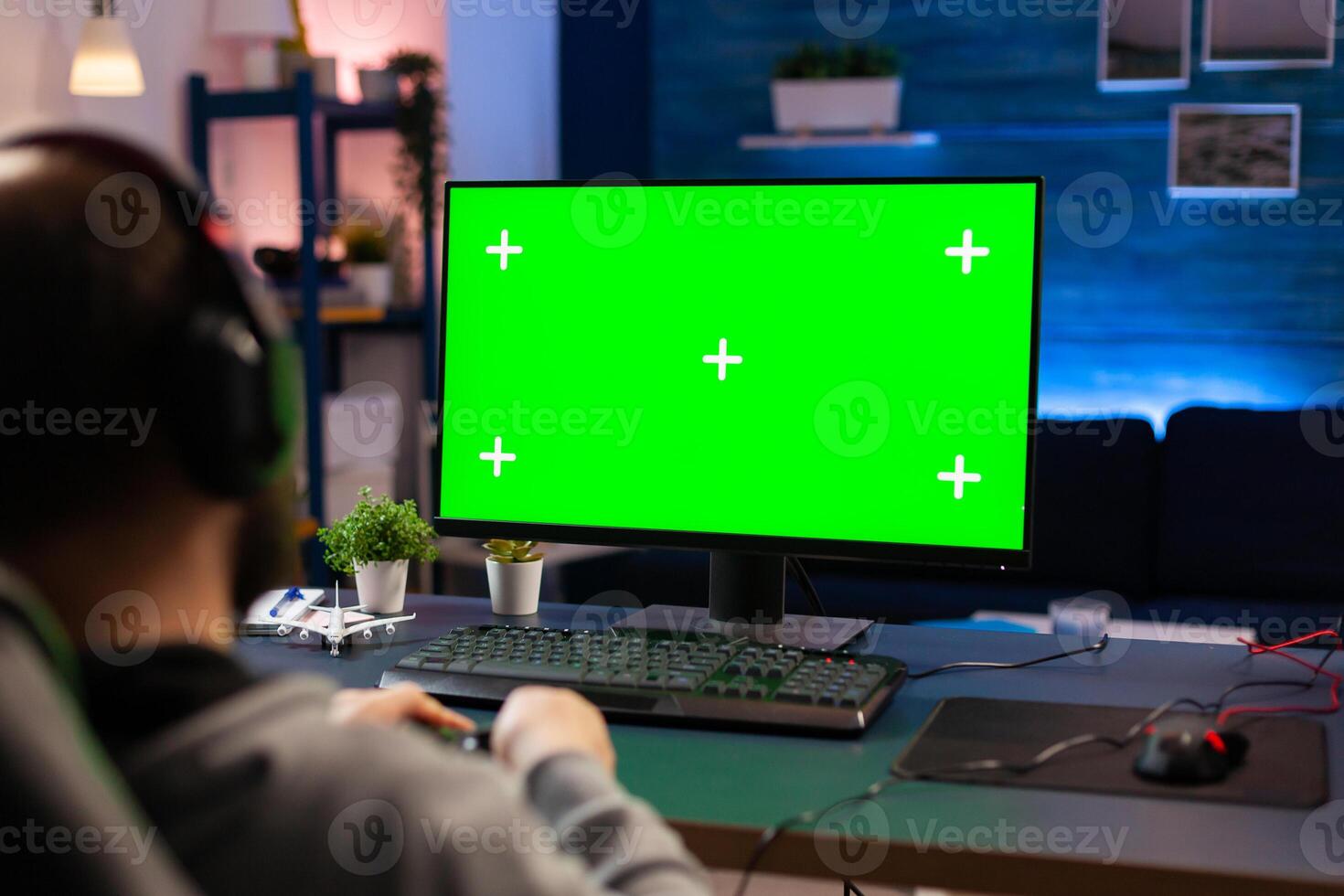 Professional player streaming videogames with green screen mock-up computer display in gaming home studio. Gamer using pc with chroma key isolated desktop streaming shooter games wearing headset photo