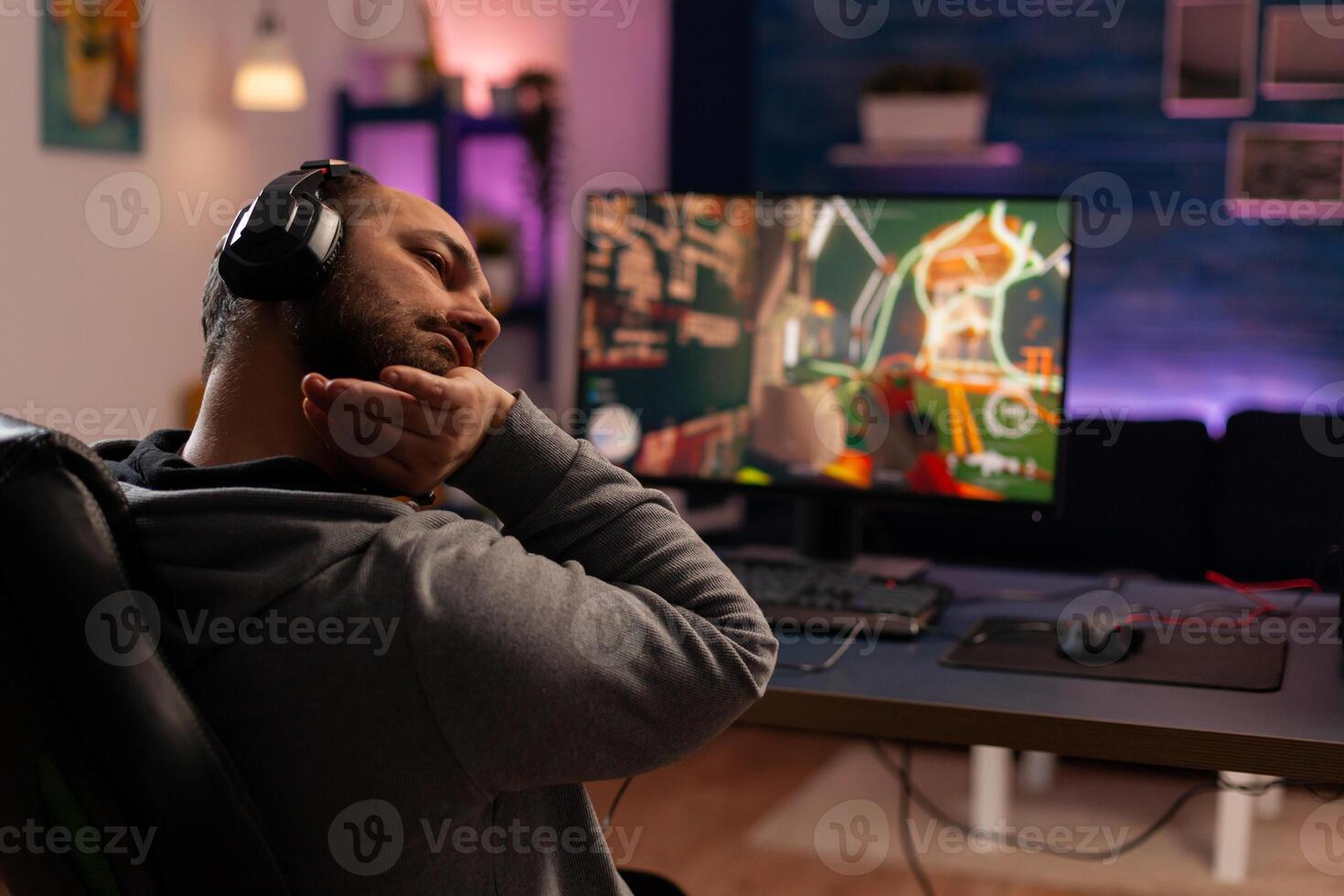 Competitive gamer streatching on gaming chair at desk and playing shooter videogames in studio home room. Online streaming cyber performing during game tournament using powerful PC with RGB photo