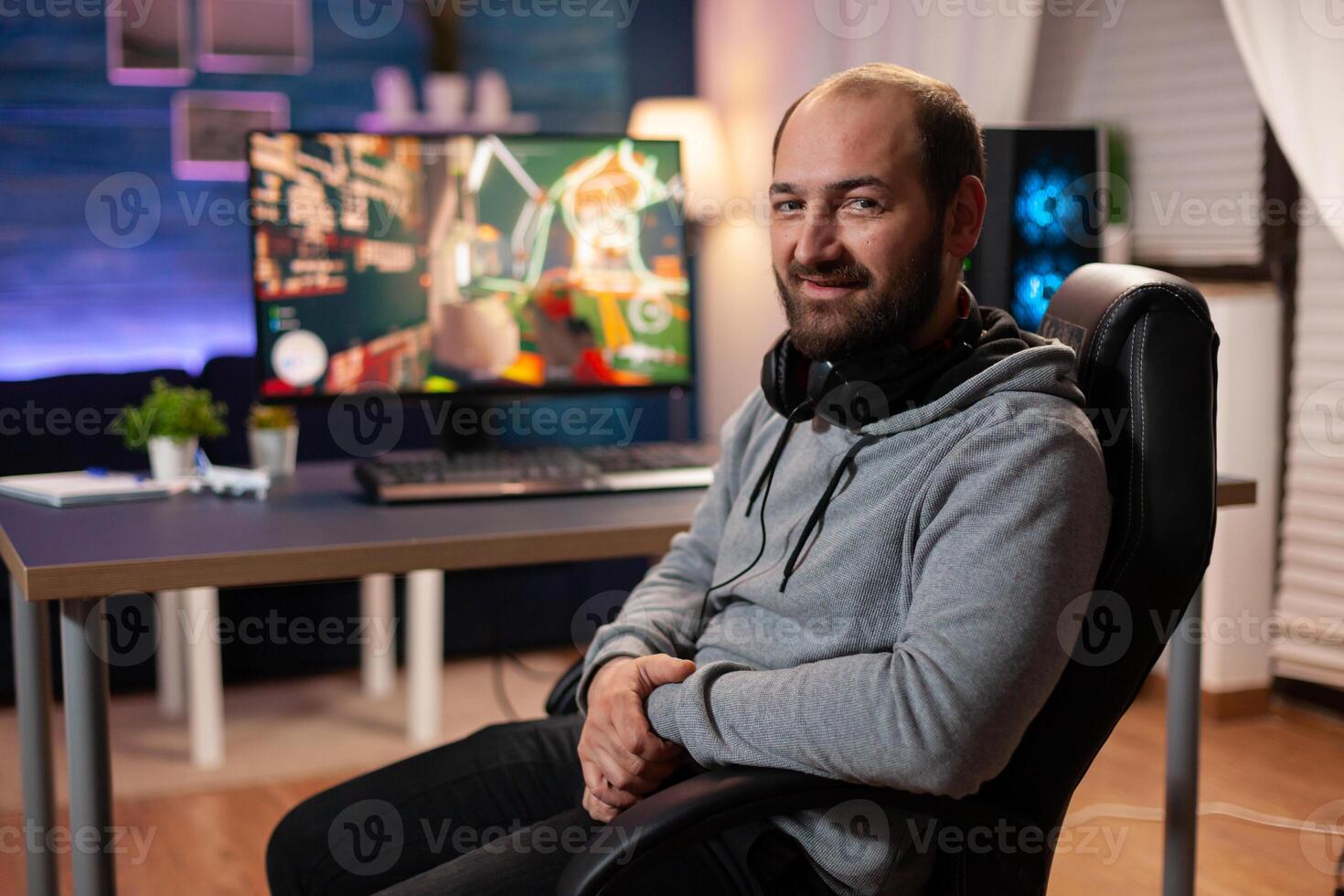 Portrait of concentrated gamer wearing professional headphones, playing online shooter game for tournament. Cyber performing on powerful pc with RGB keyword streaming videogames photo
