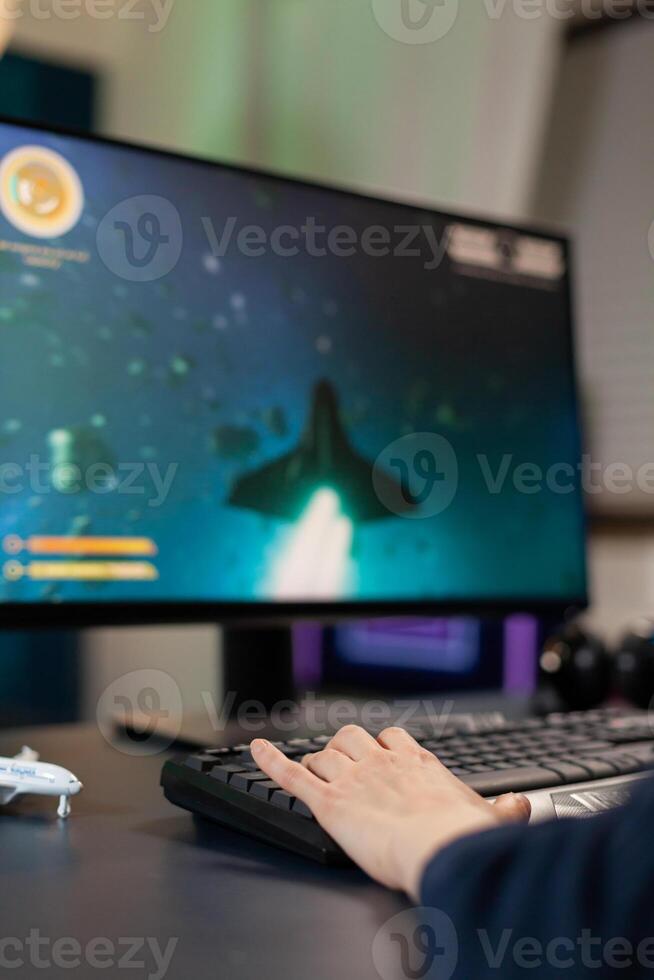 Closeup of Hand of player on professional keyboard with RGB during space shooter tournament. Pro gamer playing on gaming desk in home studio streaming online videogames photo