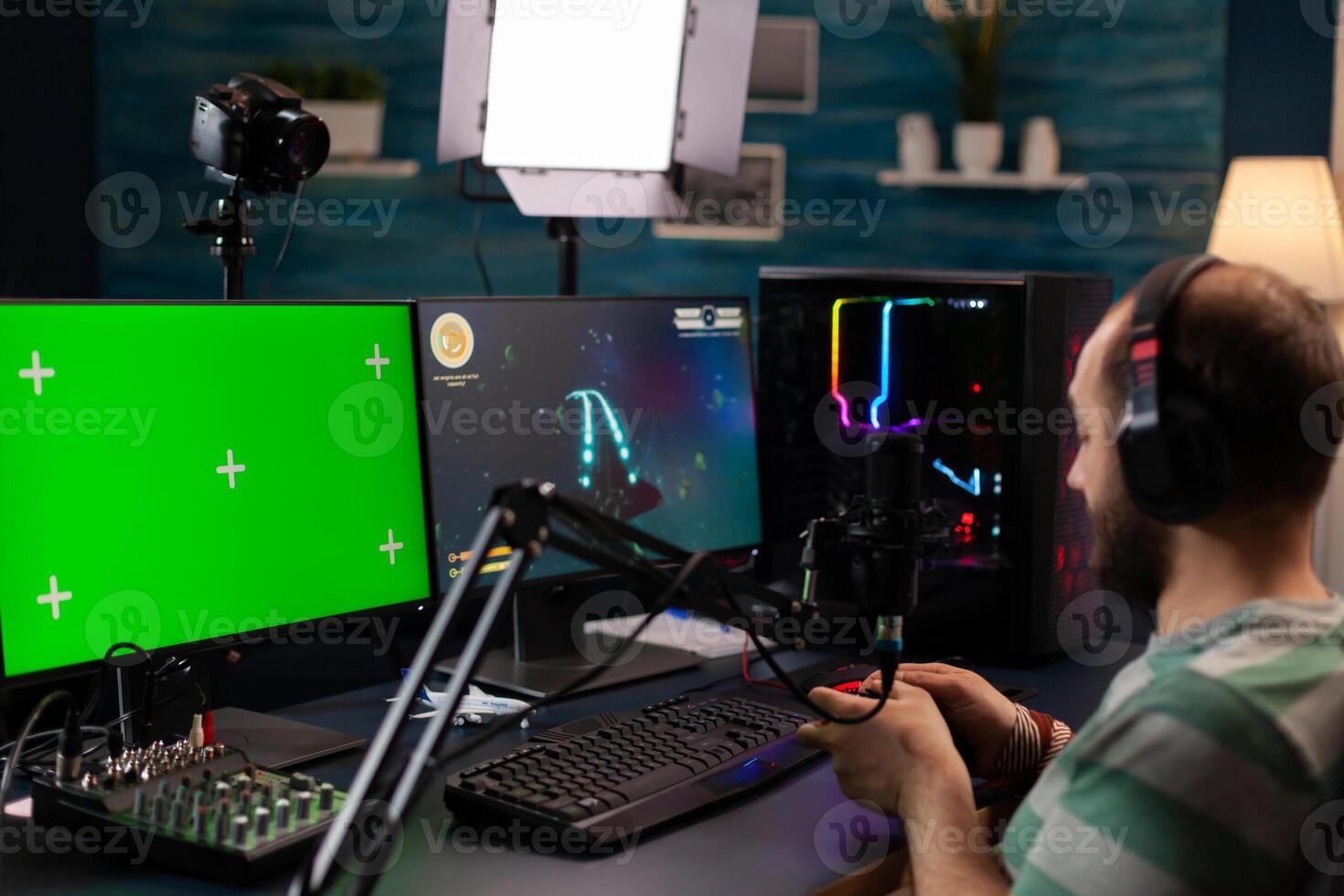 Professional cyber streamer playing digital videogames on professional powerful computer with green screen display. Player using pc with mock up chroma isolated desktop streaming shooter games photo