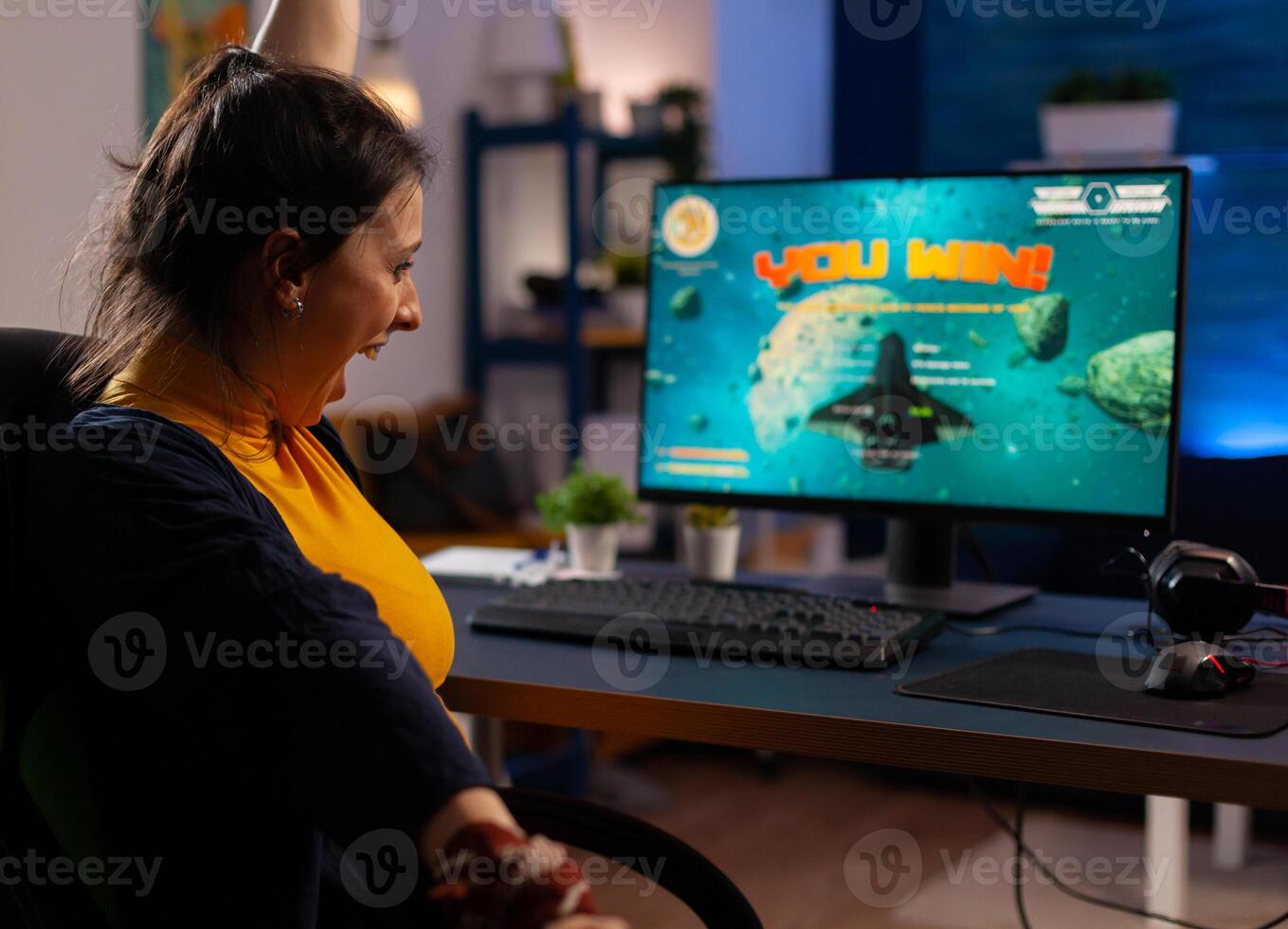 Winner player sitting on gaming chair at desk and playing space shooter games with joystick. Woman streaming online videogames for esport tournament in room with neon lights photo