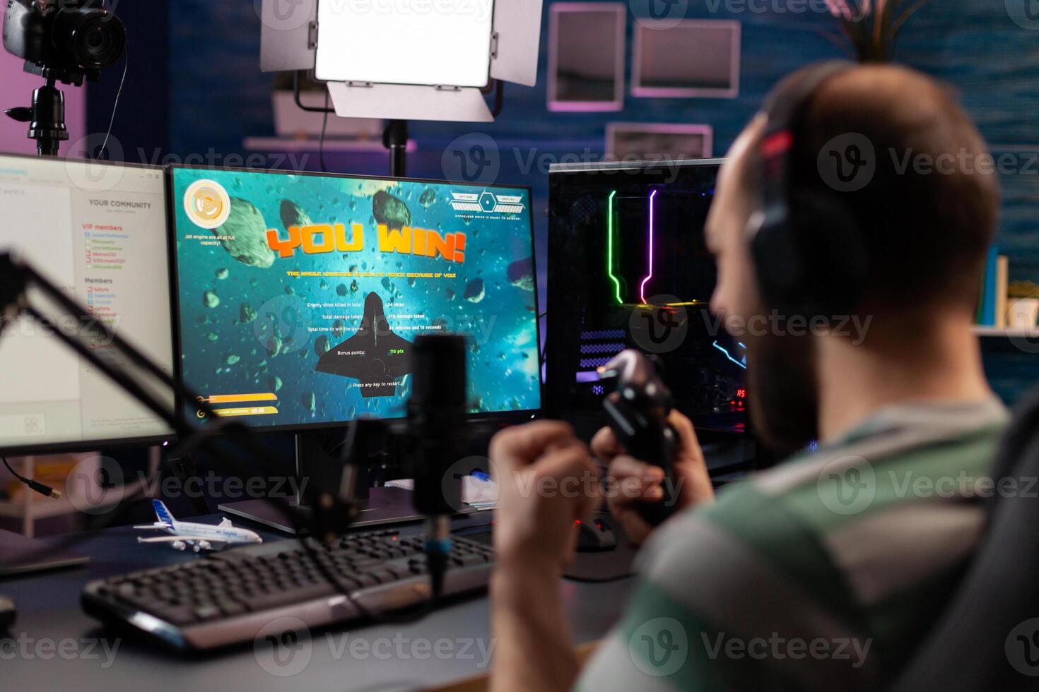 Over shoulder footage of professional streamer playing digital videogames on computer using headphones, microphone and controle. Streaming Man raising hands for wining space shooter game photo