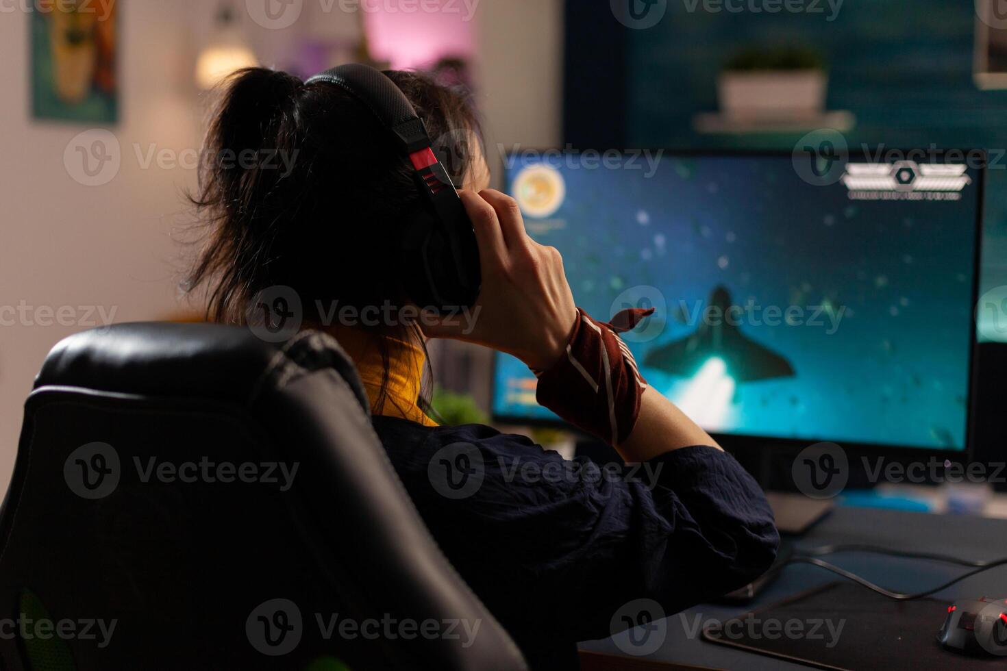 Woman videogamer using powerful computer playing online videogames in gaming home studio. Virtual streaming cyber uwearing headphones performing gaming tournament using professional equipment. photo