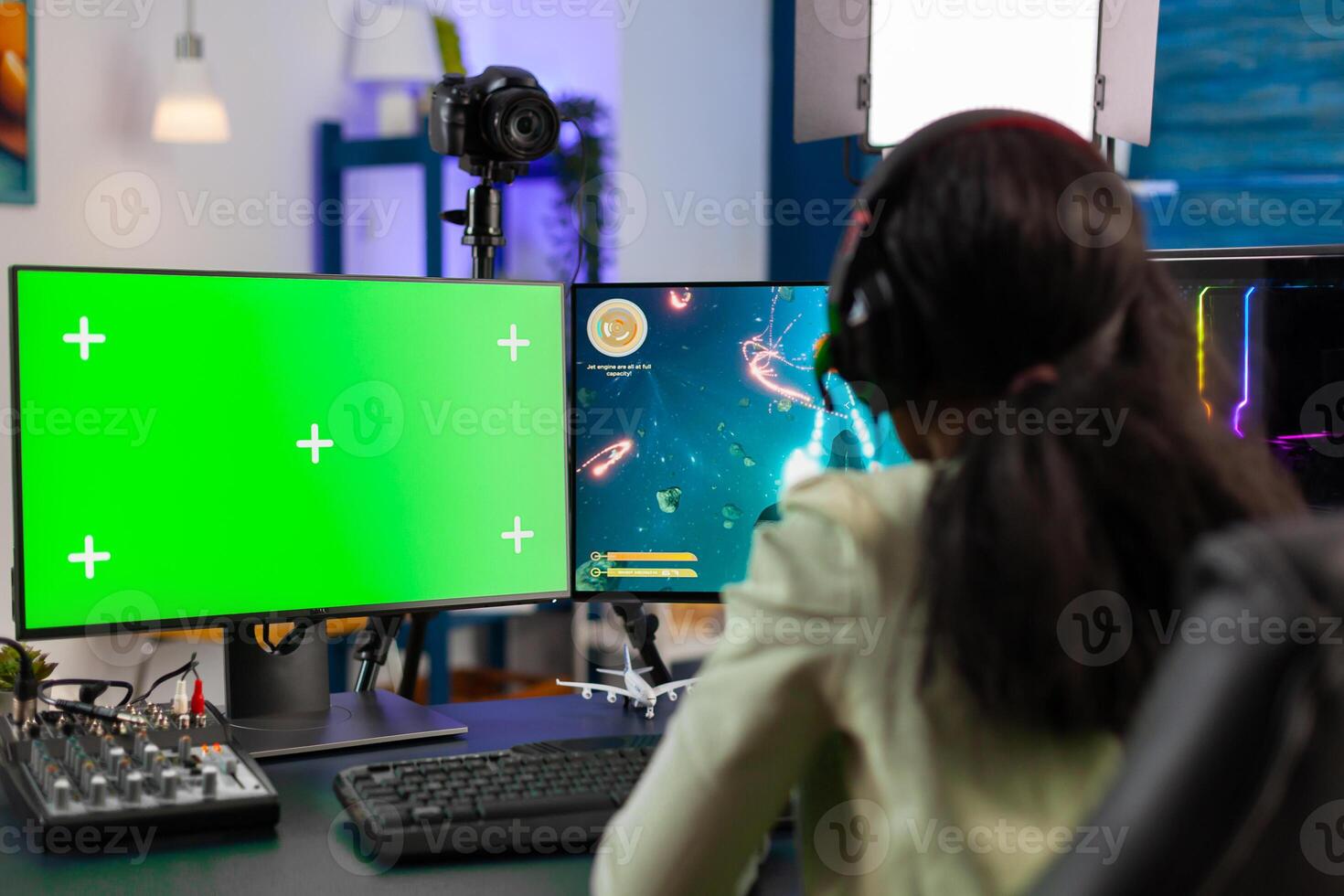 Back view of black gamer streams online game tournament on computer with green screen at night. Gamer using pc with greenscreen isolated desktop streaming space shooter games. photo