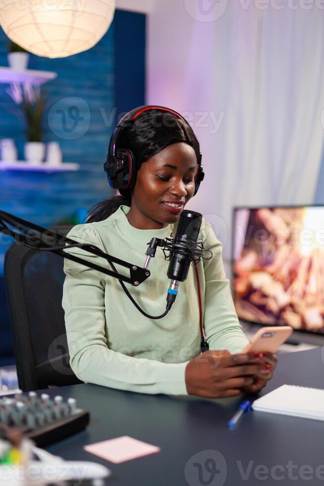 Internet show host answering at questions of fan texting on phone and talking at microphone from home podcast studio. Show production broadcast presenter streaming live content recording digital media photo