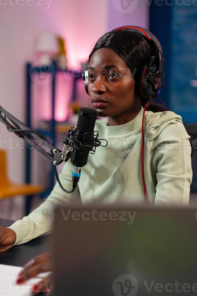 African influencer answering questions while talking into microphone for listeners. Speaking during livestreaming, blogger discussing in podcast wearing headphones. photo