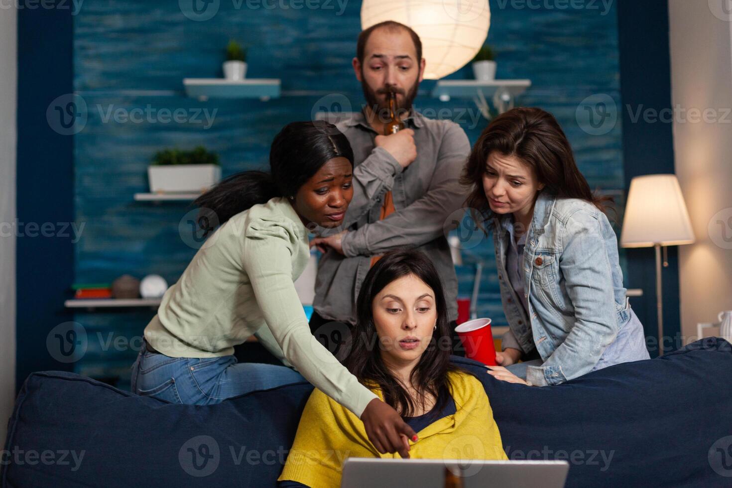 Multi ethnic people socialising drinking alchool talking with friend on call. Group of multiracial people on conference call, chat party on laptop during night life entertainment photo