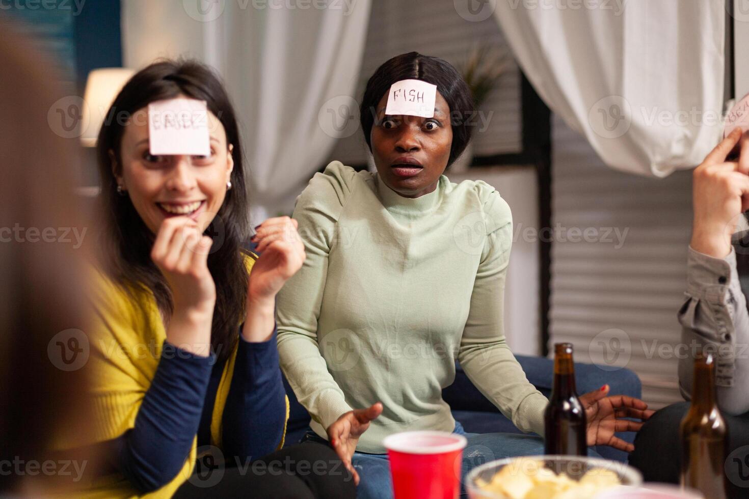 Group of multi-ethnic people having fun while playing board game using sticky notes spending time together. Creative friends hanging out late at night in living room during home party. photo