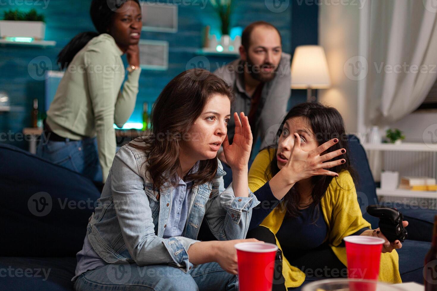 Woman upset after lose at online games while having socializing with multi ethnic group of friends in home living room late at night, drinking beer. photo