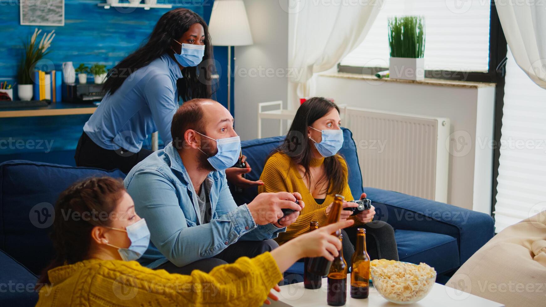 Sad friends because loosing playing games with wireless controller wearing face mask to prevent getting sick with corona in time of social pandemic. Group of people enjoying time together. photo