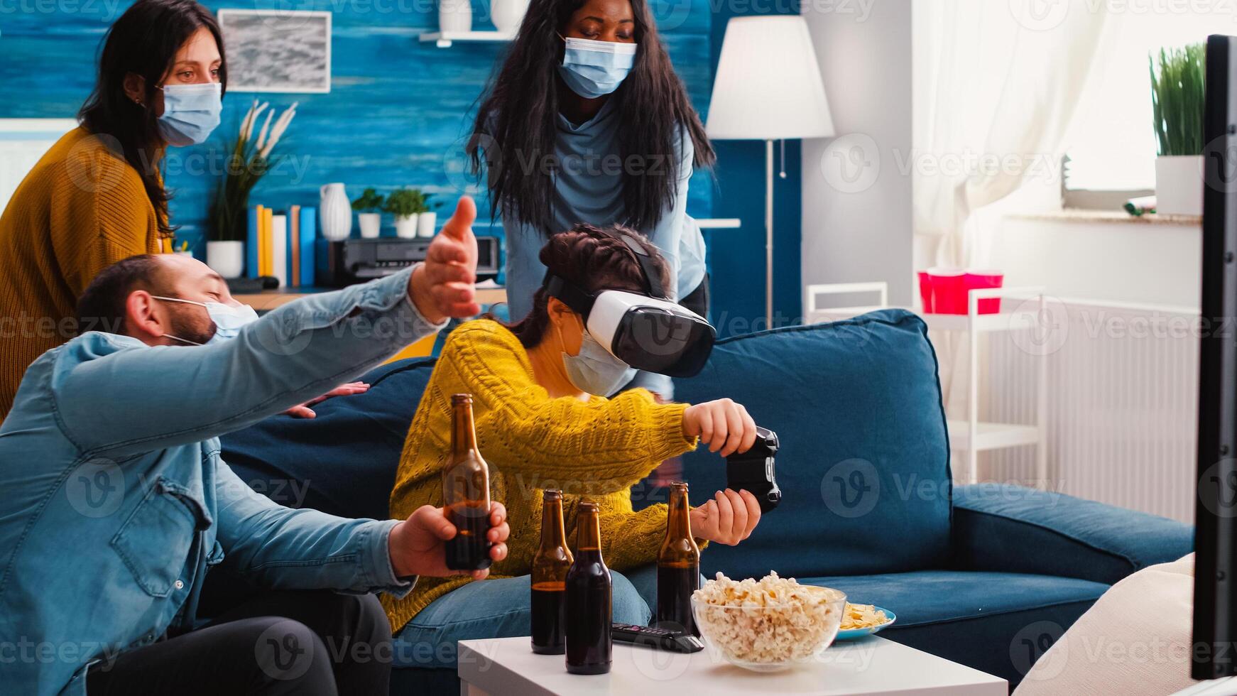 Group of multiethnic friends having fun playing game experiencing virtual reality headset keeping social distancing in home living room due to social pandemic. Diverse people in new normal party photo