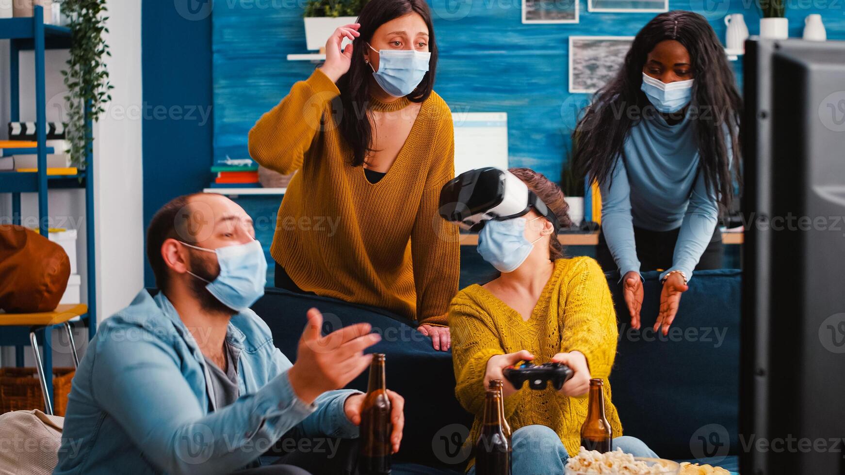 Young woman experiencing virtual reality playing games with vr headset and joystick in home living room while friends supporting her keeping social distancing because of global pandemic. photo