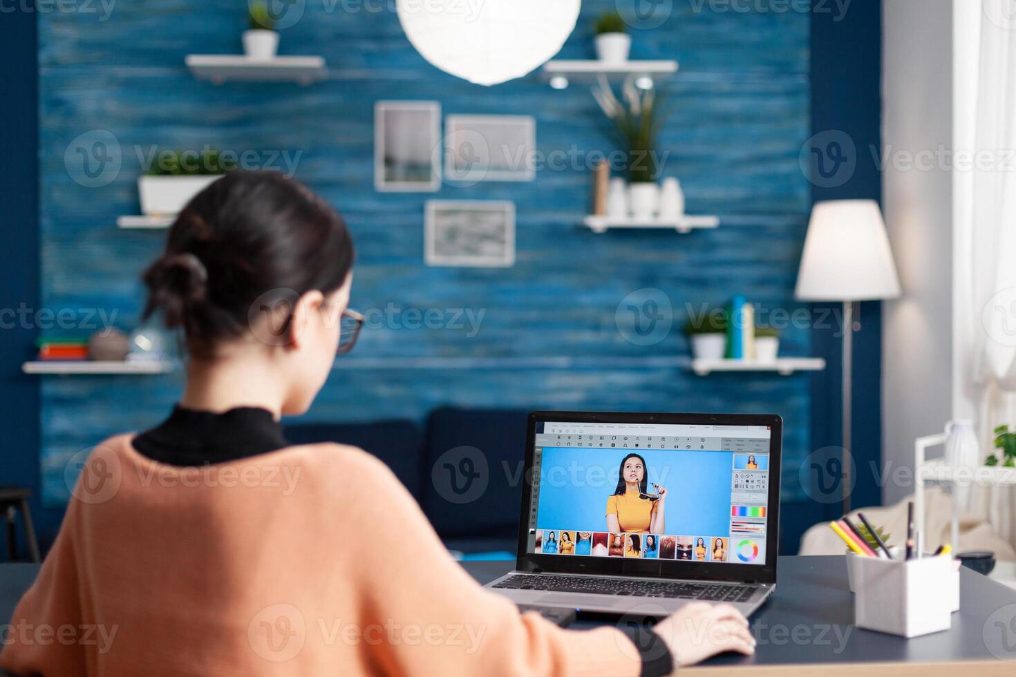 Creative photographer student editing pictures while changing color grade, retouching photos using laptop computer. Young editor sitting at desk table in living room studying photography design