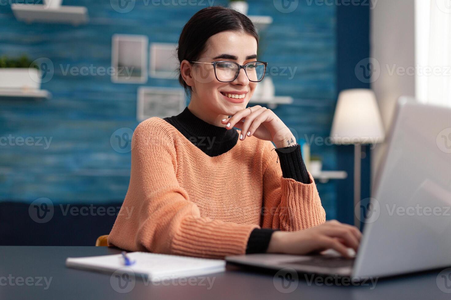 Student browsing on internet management information for university exam looking at e-learning platform. Woman doing her homework using laptop computer while sitting at desk table in living room photo