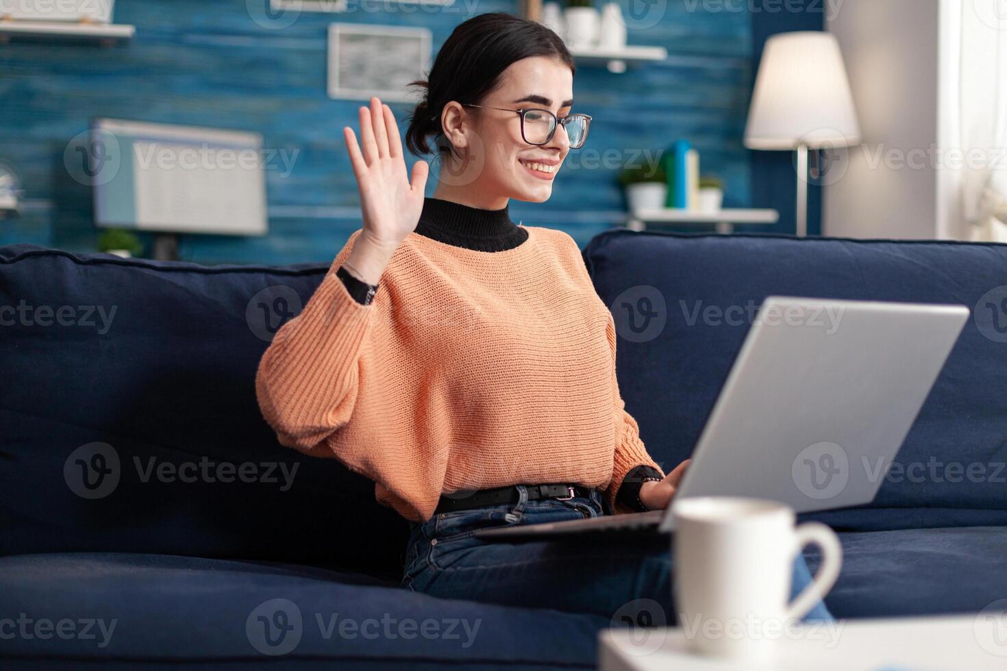 Student waving her friends during online videocall conference sitting on sofa in living room. Young woman using mobile internet web virtual webinar vlass on videoconference meeting photo