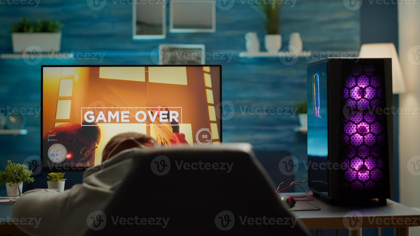 Back view of sad professional eSports gamer losing shooter mock-up game. Defeated man with headphones streaming online cyber performing during gaming tournament using powerful personal computer photo