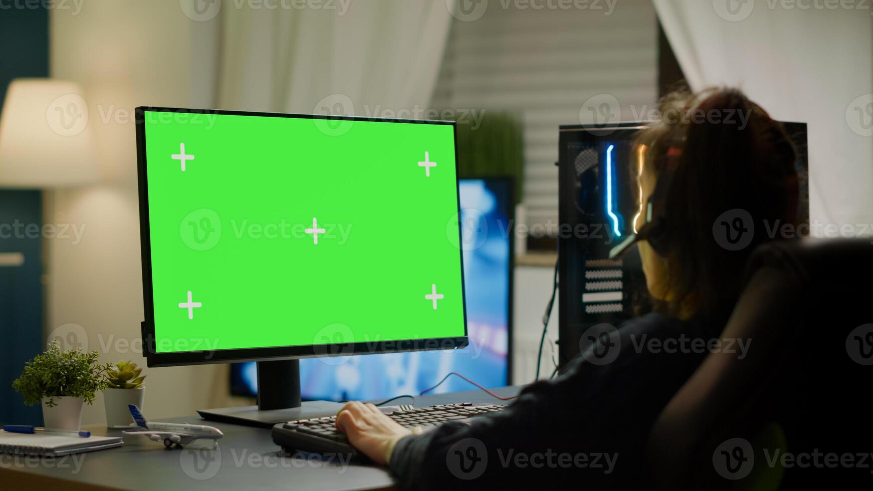 Pro gamer playing virtual game on powerful computer with green screen mock up, chroma key display. Cyber player using professional pc with isolated desktop streaming shooter games wearing headset photo