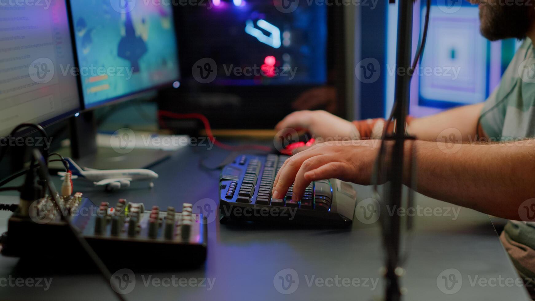 Close up of streamer typing at RGB keyboard playing space shooter videogame. Pro cyber man using mixer sound in gaming home studio for online esports competition on professional powerful computer photo