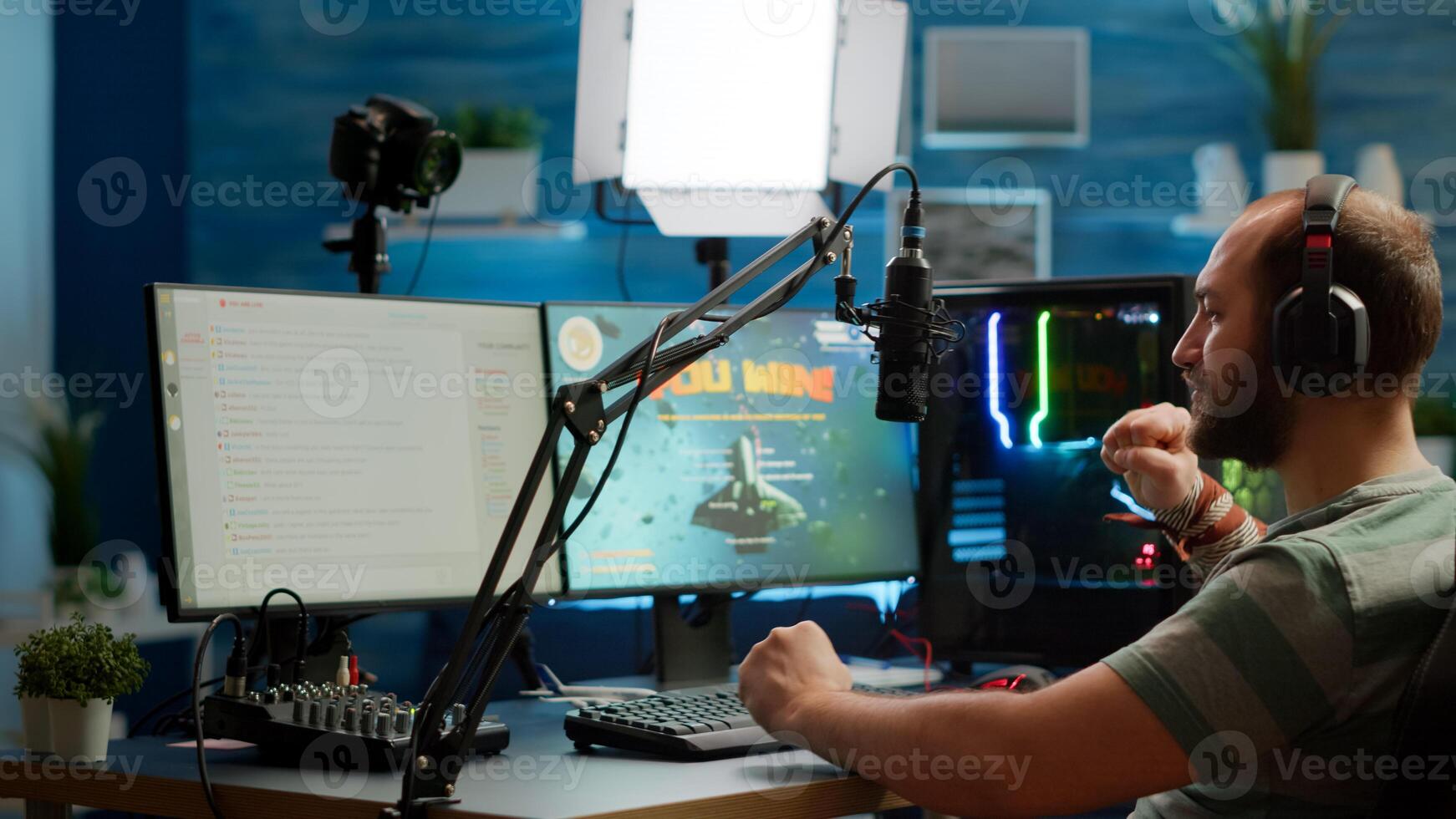 Streamer man talking with multiple players into headphones and winning games competition. Professional gamer streaming online videogames with new graphics on powerful computer from gaming room photo