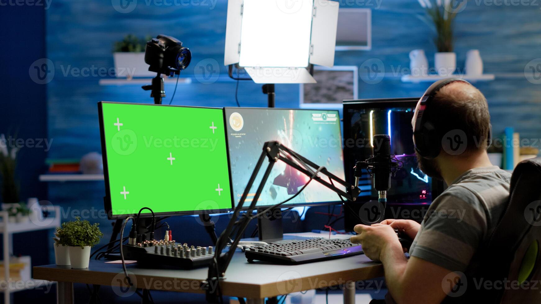 Gamer streaming online videogames on professional powerful computer with green screen, mock up, chroma key display. Streamer playing space shooter game at isolated desktop holding wireles controller photo