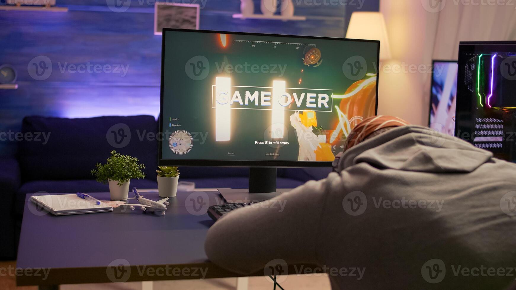 Over shoulder shot of man after losing at games on computer using professional RGB equipment. Defeted player playing first person shooter games using modern technology network wireless photo