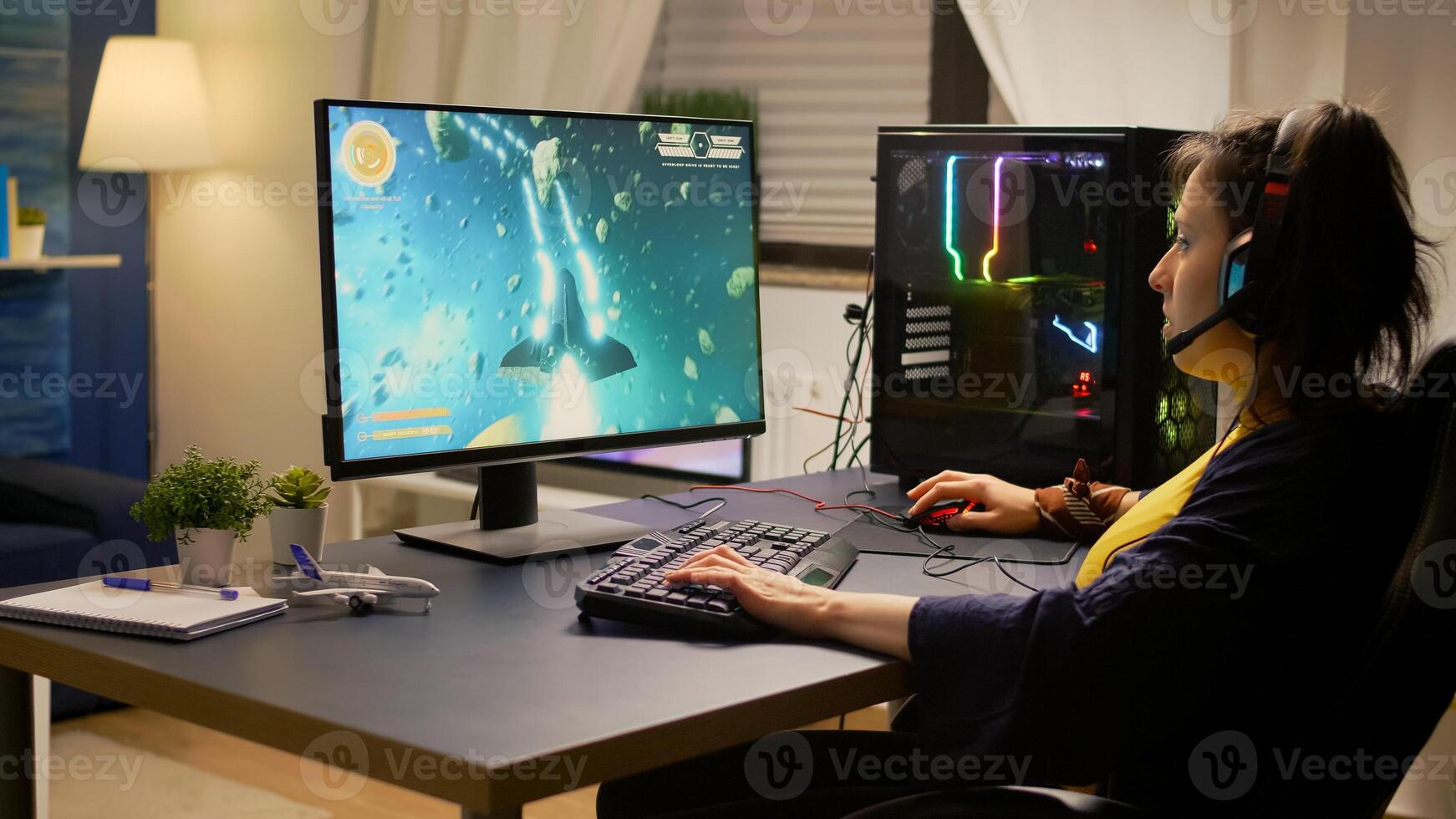 Gamer playing online space shooter games using powerful computer and RGB keyboard. Player wearing headphones and talking into microphone with other players for winning online tournament photo
