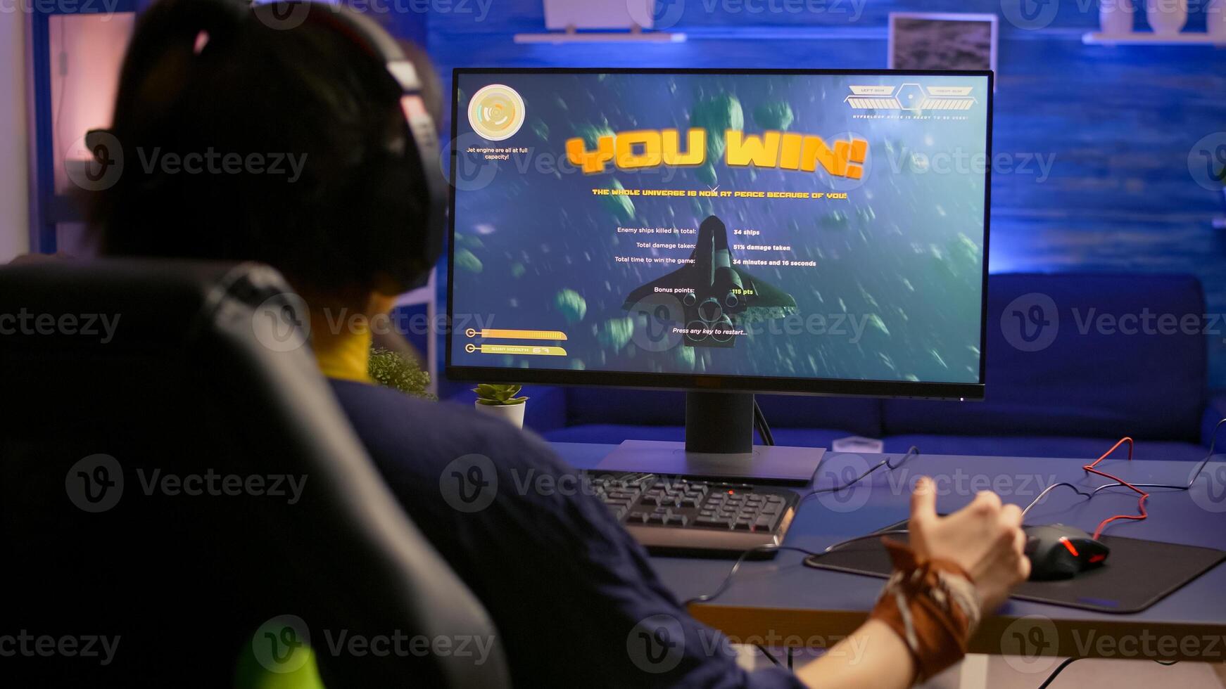Excited pro gamer with professional headphones making winner gesture while playing space shooter games. Player streaming digital games during online competition using RGB system desktop photo