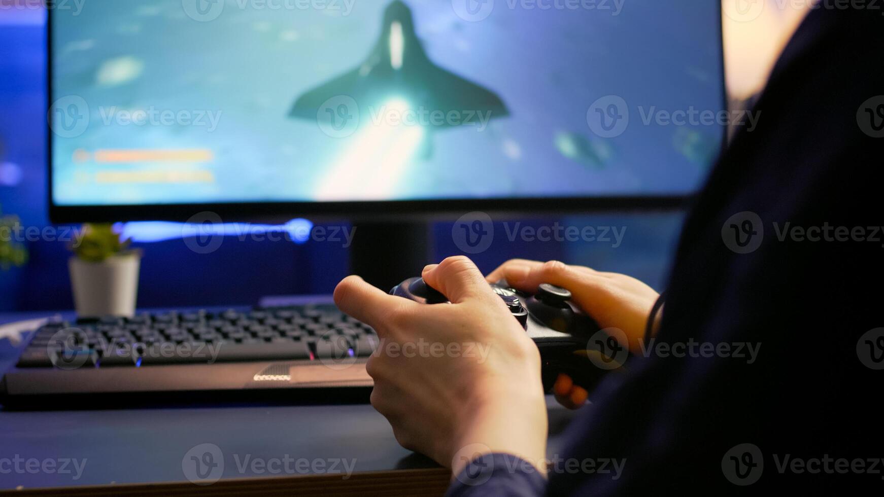Close-up of professional cyber gamer playing space shooter game using wireless controller. Pro player use RGB equipment during gaming tournament late at night in home studio photo
