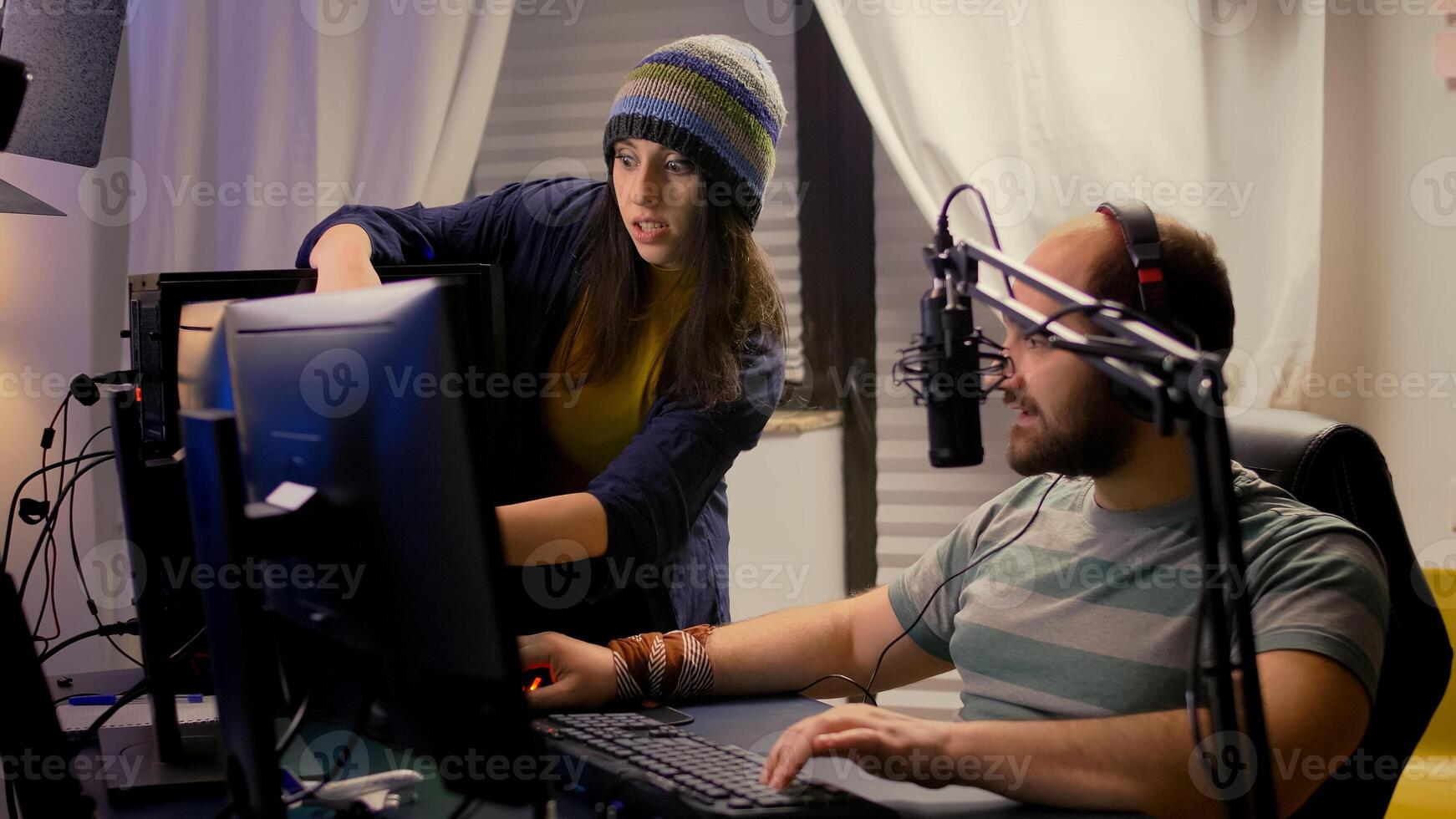 Girlfriend supports her pro gamer boyfriend, playing online game using streaming professional equipment. Streamer talking into microphone with multiple players during gaming tournament photo