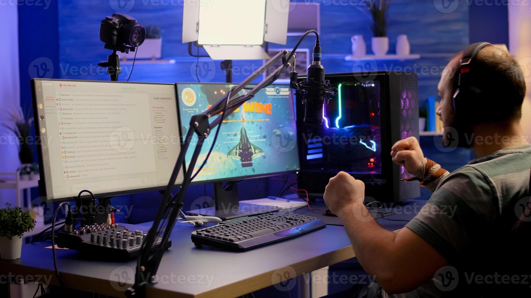 Streamer man winning space shooter online competition using professional microphone, keypad, mouse in gaming home studio. Player playing online games with streaming chat open during tournament photo