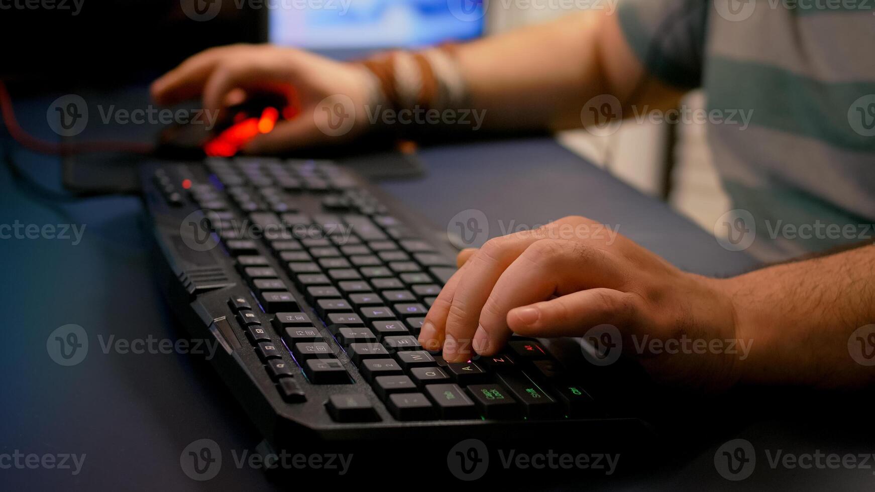 Close-up of streamer man playing space shooter game using RGB keyboard during esport tournament. Player performing online competition late at night in streaming home studio photo