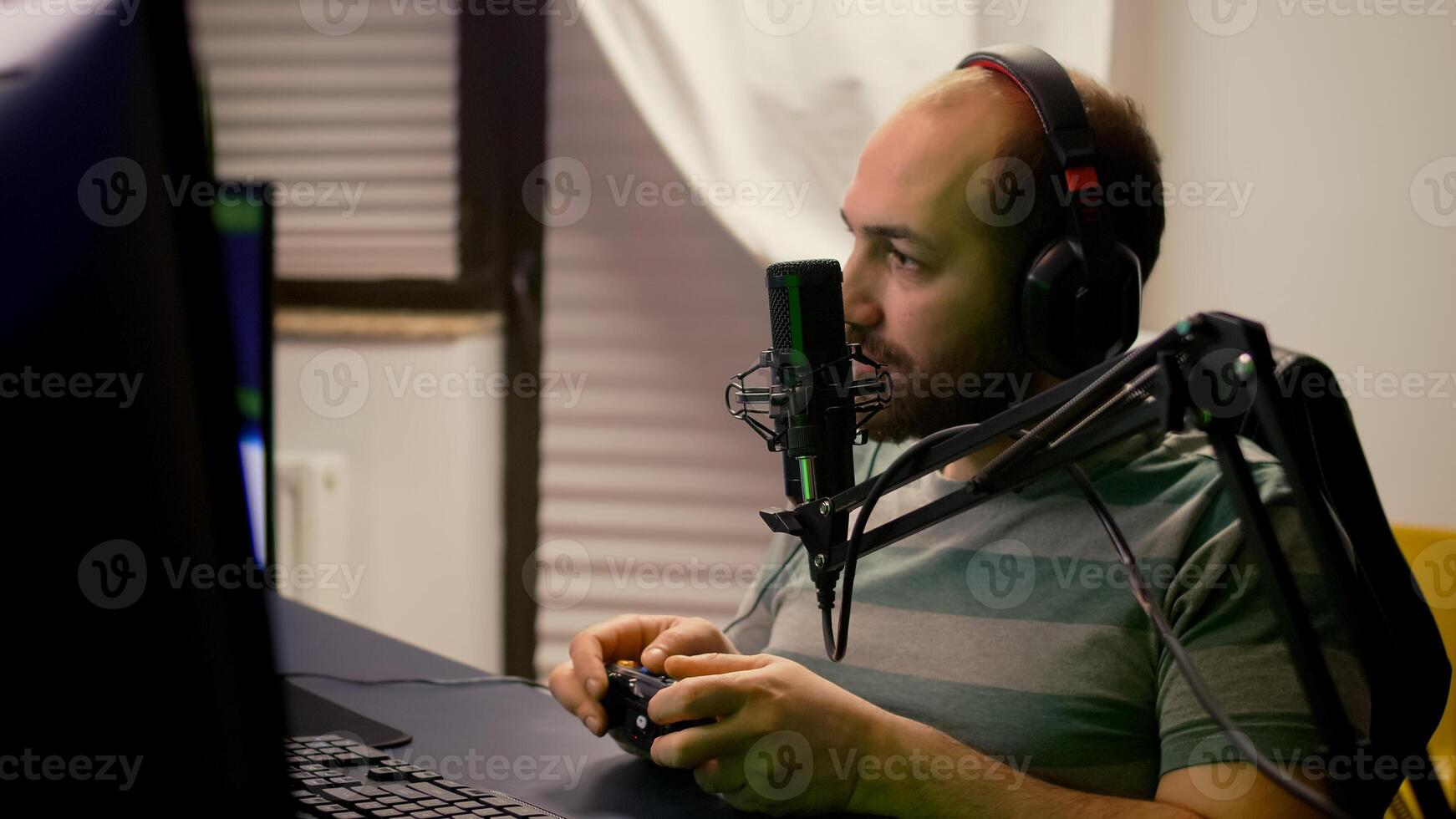Close-up of pro streamer talking into professional microphone during virtual competition. Player streaming online games using wireless controller late at night in gaming home studio photo