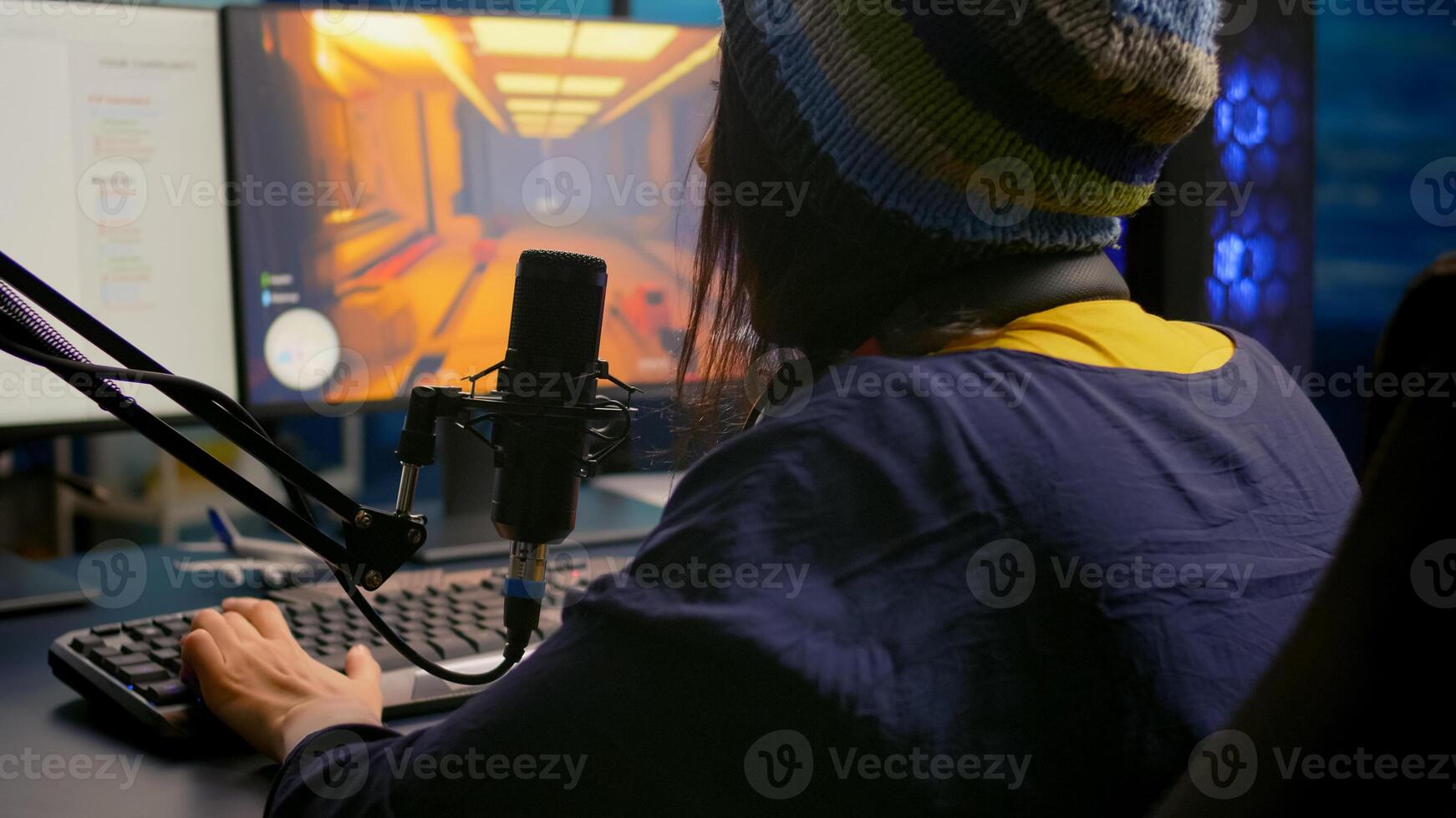 Back shot of pro gamer woman playing first person games using RGB keyboard in home studio. Gamer streaming gameplay using professional gaming equipment during online competition photo