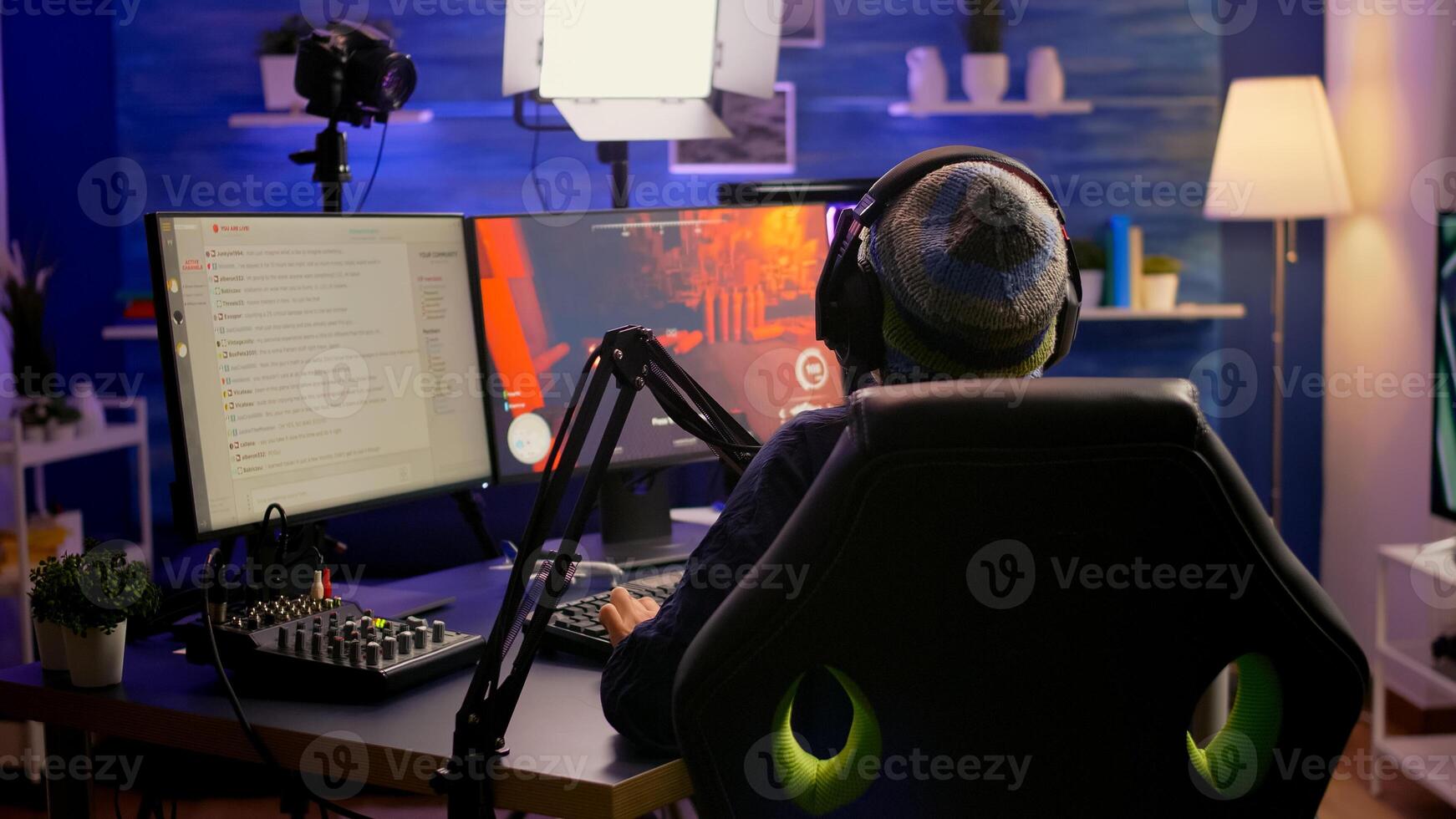 Back shot of pro streamer with headphone playing first person shooter game competition use RGB keypad. Player sitting on gaming chair using streaming equipment late at night in home studio photo