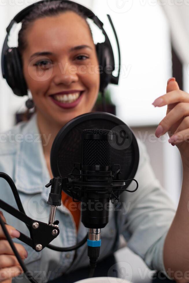 Closeup of smiling woman influencer talking into microphone. Vlogger with headphones using recording gear for live broadcast. Audio streaming equipment for internet online radio production. photo