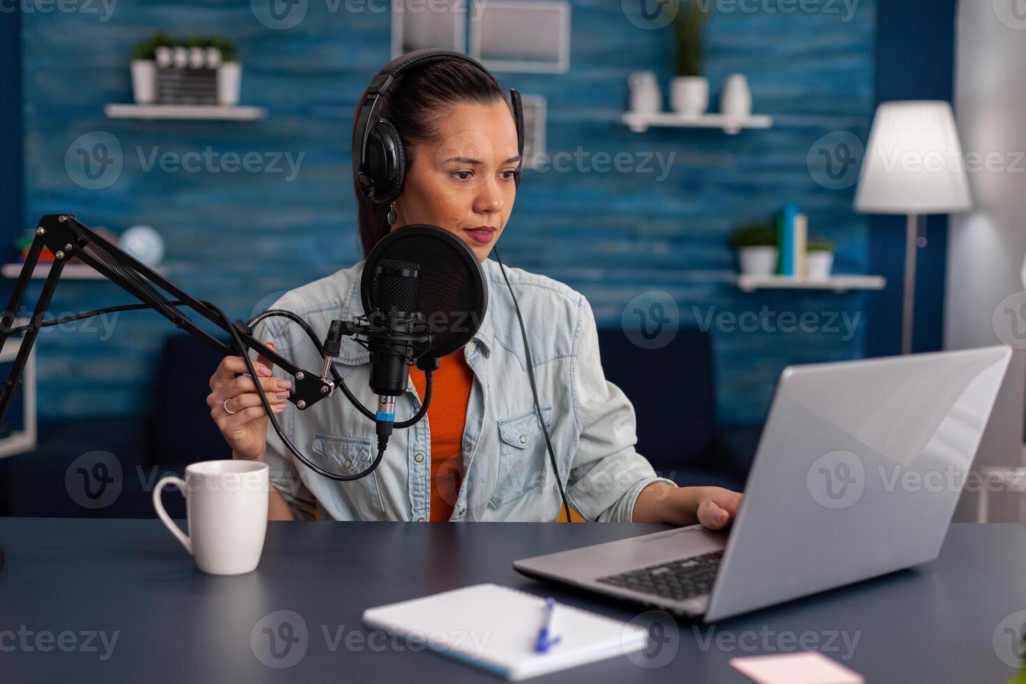 Woman vlogger streaming podcast and using laptop at desk. Influencer with headphones in home office recording livestream on computer. Blogger live broadcasting for social media with microphone. photo