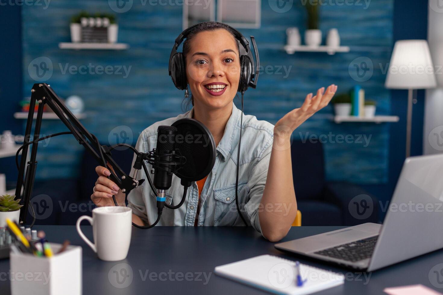 Portrait of woman smiling at camera in home recording studio. Vlogger with headphones creating content for online social media. Influencer streaming podcast using microphone and laptop. photo