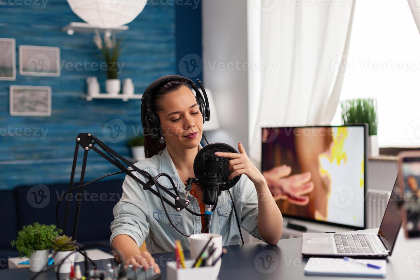 Content creator touching microphone to test sound. Vlogger testing audio equipment with finger. Woman influencer with headphones in home studio doing sound check for online podcast. photo