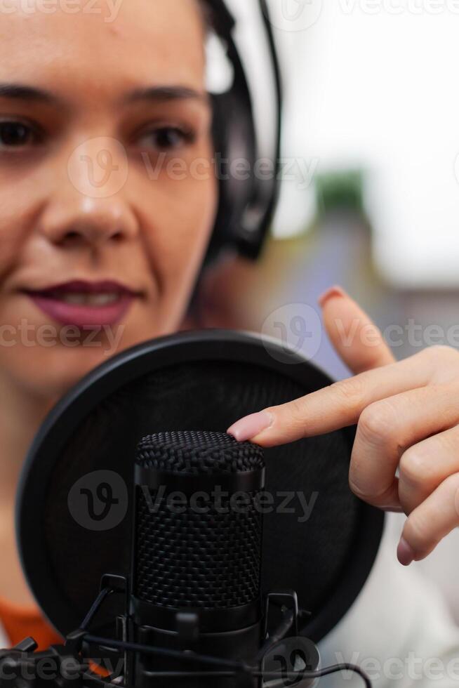 Closeup of influencer with headphones testing microphone sound. Woman content creator touching audio equipment with index finger. Sound check for online podcast streaming on social media. photo