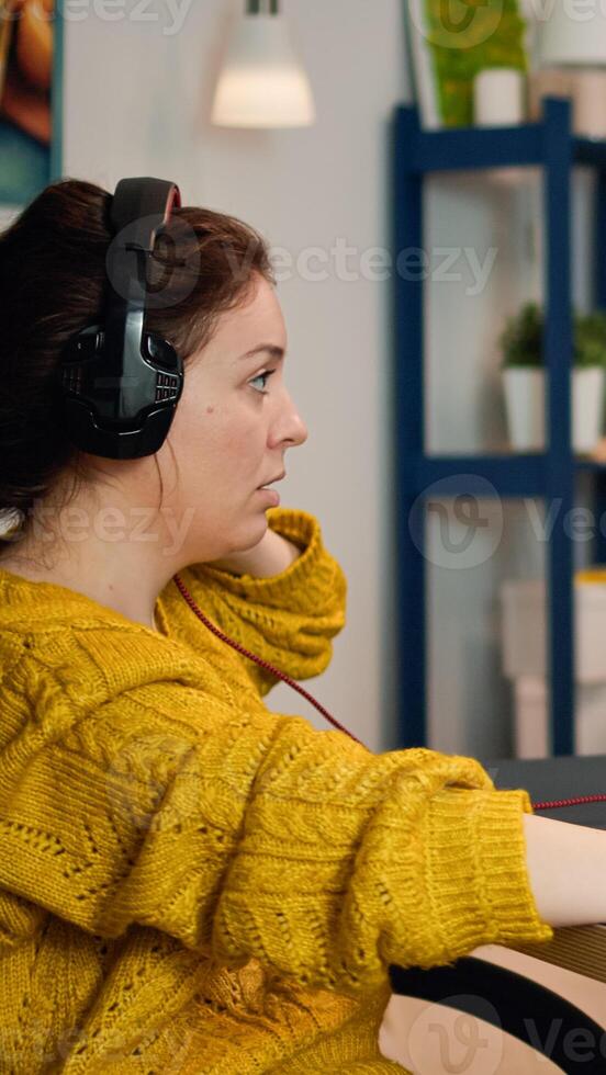 Focused woman gamer sitting on desk, putting on headset with a mic and starts playing game. Online streaming cyber performing on powerful personal computer during gaming tournament photo