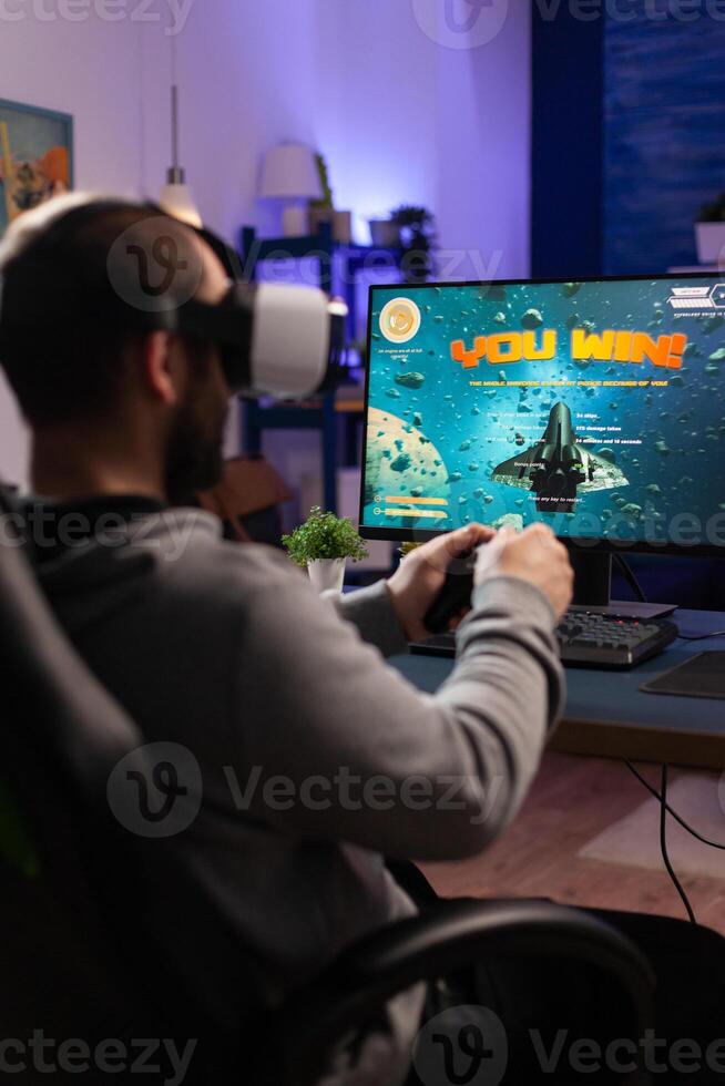 Gamer playing games with controller and vr headset. Player winning game while he uses joystick and virtual reality glasses on computer. Gamer feeling happy about online win. photo