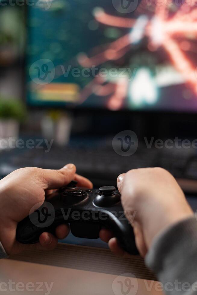Close up of gamer holding controller to play games in front of computer. Player using joystick and playing online games on monitor, sitting at desk. Man gaming with modern equipment. photo