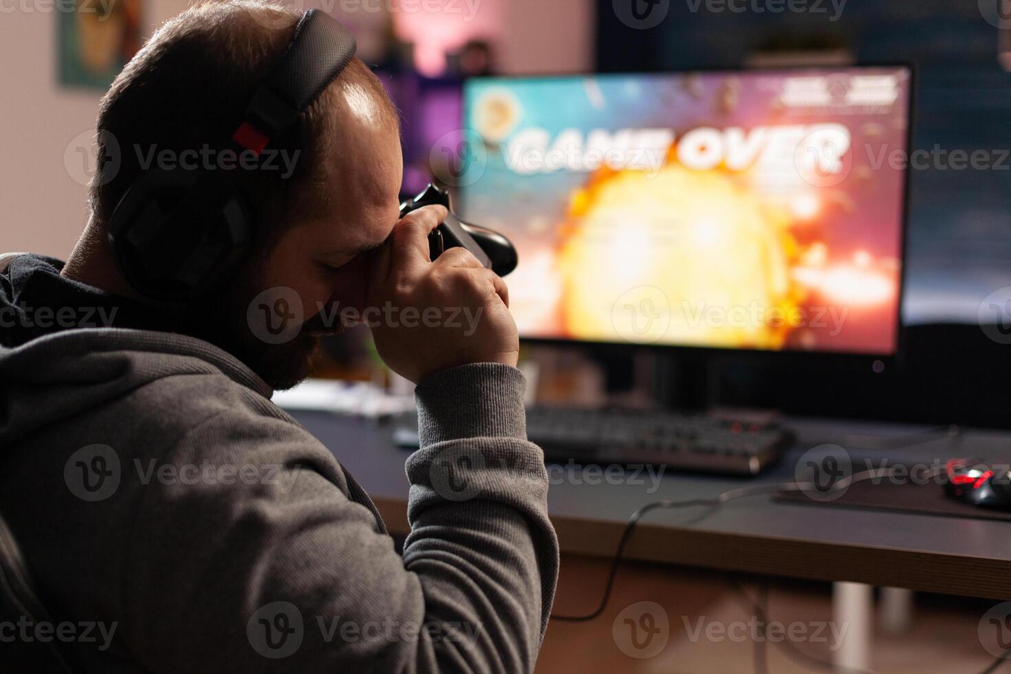 Sad man losing games after playing with joystick and headphones on computer. Gamer feeling disappointed about lost game, using controller and headset. Person gaming with equipment photo