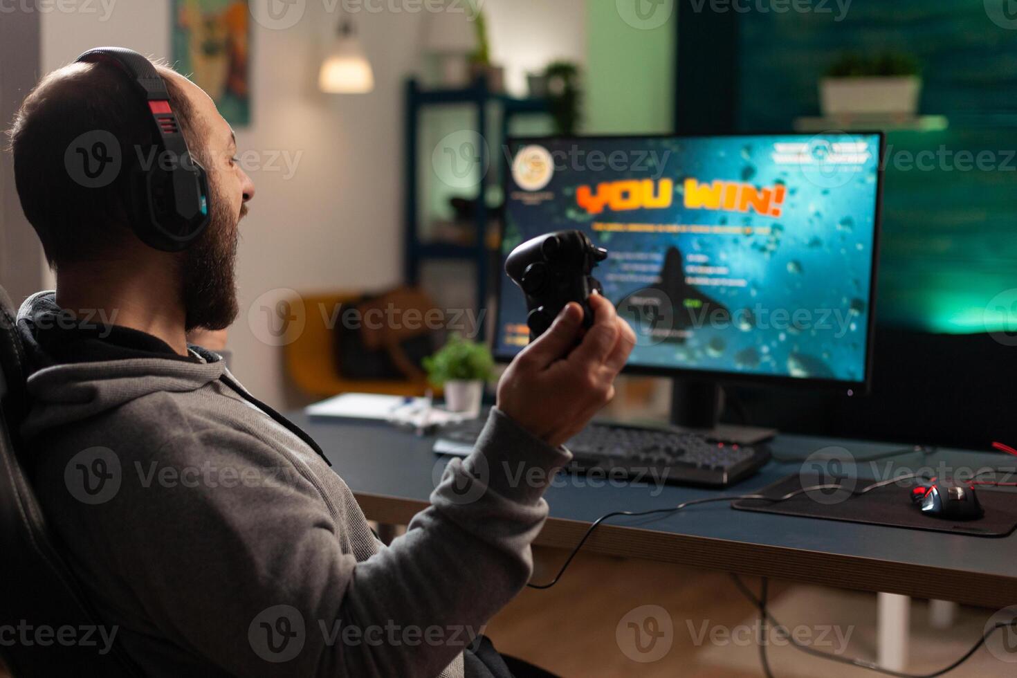 Player winning games with controller and headset in front of monitor. Man using joystick and headphones, playing online games on computer. Person celebrating game win for leisure. photo