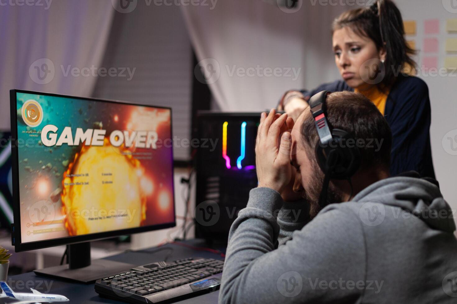 Couple of gamers feeling sad about losing games in front of computer. Woman comforting man about lost game online, having gaming equipment and headphones to play for leisure. photo